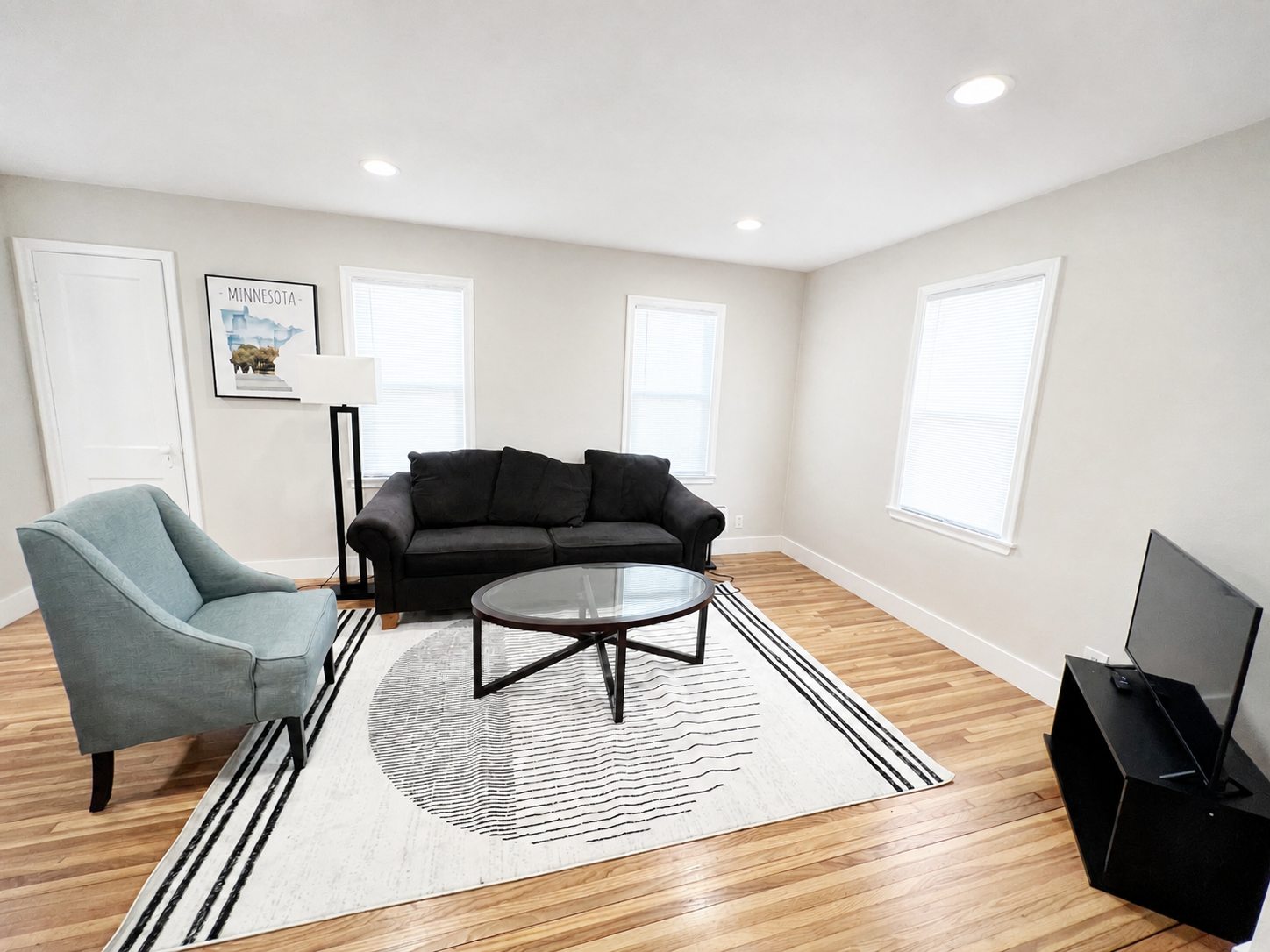 Lower-home living room with sofa, chairs, television, and hardwood floors